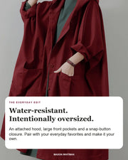 Oversized water-resistant windbreaker editorial card: attached hood, large front pockets, snap-button closure.